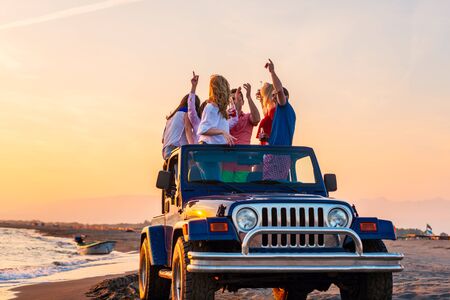 Young group having fun on the beach drink beer and dancing in a convertible carの写真素材