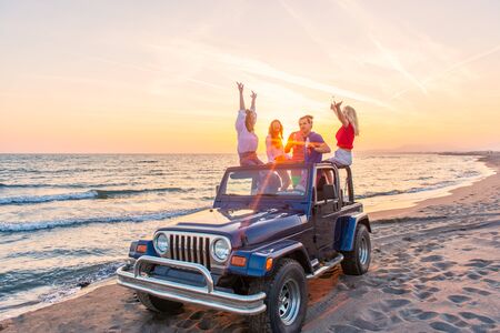 Young group having fun on the beach drink beer and dancing in a convertible carの写真素材