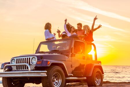 Young group having fun on the beach drink beer and dancing in a convertible carの写真素材