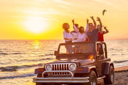 Young group having fun on the beach drink beer and dancing in a convertible carの写真素材