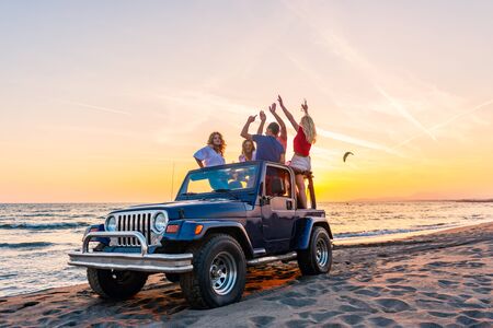 Young group having fun on the beach drink beer and dancing in a convertible carの写真素材
