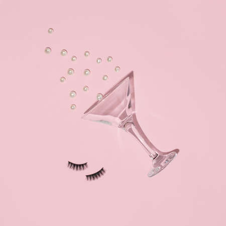 Creative layout with martini cocktail glass, false eyelashes and white pearls on pastel pink background. Retro fashion style. Aesthetic party or celebration concept. Happy girl life idea.の写真素材