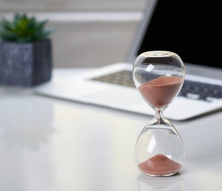 Hourglass on office desktop with supplies. White background. Copy space for text. 