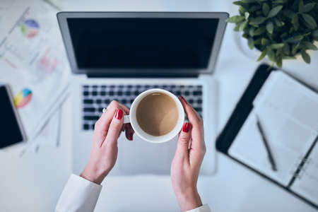 Top view image of woman holding coffee at the office desk over the laptop.の写真素材