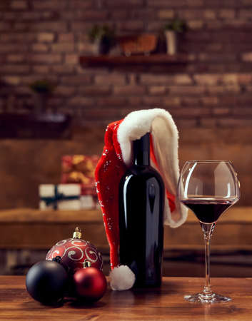 Christmas decorations and wine glasses and a bottle of red wine on table at home dark living room in background. Winter mood with dark and warm colors.の写真素材
