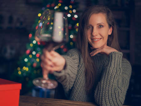 Beautiful woman toasting with red wine. Selective focus. Christmas lights in the background.の写真素材