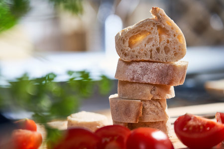 Sliced bread, baguette on wooden cutting board at home in the kitchen, with red tomato. Close-up image of bread slices. Cooking, food and home concept.の写真素材