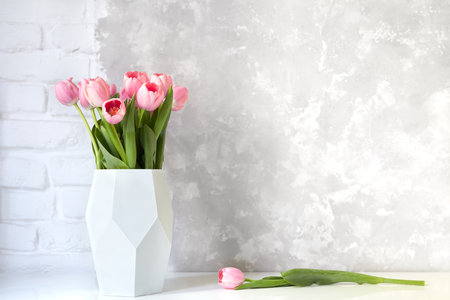 Pink tulip bouquet in vase on white table on white brick wall and bright concrete background. Copy space for text.の写真素材