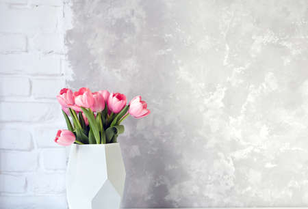 Pink tulip bouquet in vase on white table on white brick wall and bright concrete background. Copy space for text.の写真素材