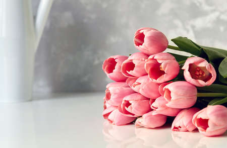 Close up image of beautiful pink tulip bouquet on white table with vase in the background in bright room.の写真素材