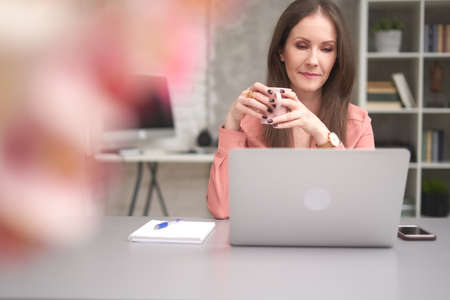 Business woman holding coffee while working, using laptop computer in the office.