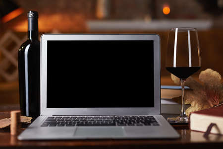 Empty blank screen laptop computer on table with wine bottle wine rack holder in the background....
