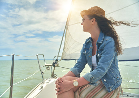 Happy young woman enjoying cruising on a sailboat on a sunny cloudy summer day.