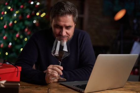 Handsome man drinking wine, using laptop, shopping online, having video chat on laptop computer. Christmas tree in the background.の写真素材