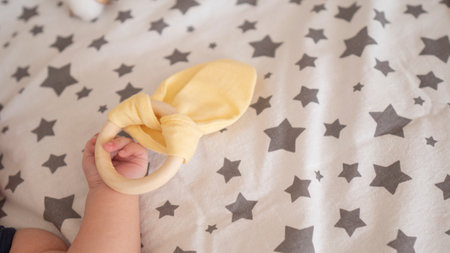 New born tiny hand with wooden textile toy on a pastel white napkin. Unrecognizable girl kid laying in the bed. Close up, copy space. childcare and maternityの写真素材