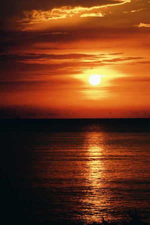 Tropical beach at sunset with sun over oceanの写真素材