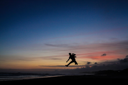 silhouette of people jumping on the beach with their hands clenchedの写真素材