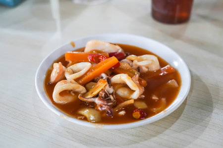 Cumi Asam Manis, Sweet and Sour Saute Squid with Red Paprika Served on White Plate above the Tableの写真素材
