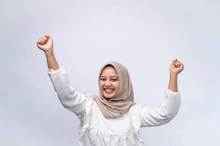 Excited beautiful Indonesian Muslim woman wearing hijab celebrating success and looking at camera isolated on white background. People religious lifestyle conceptの写真素材