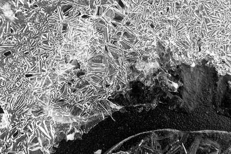 The texture of the ice crust on the pavement, black and white photo, broken lines on texture,...