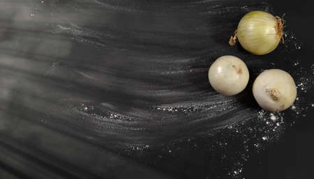Black background sprinkled with flour, smeared flour, table for cooking, rolling dough. Three unpeeled onions, sunbeams on the left. Blank space for menu text, recipe, ingredients.の写真素材