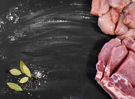 Raw pork pieces, chicken fillet, bay leaf, salt sprinkled on a black background of a table sprinkled with flour. Background with empty place for text menu, recipe.の写真素材