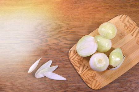 Peeled onions on a wooden cutting board, a few slices of onion on a wood-textured table, sun light on the left. Empty space for menu text, recipe, banner.の写真素材