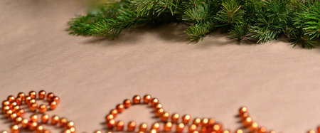 Background beige craft paper, at the top there is a strip of spruce green branches, bottom orange...