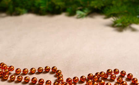 Background beige craft paper, at the top there is a strip of spruce green branches, bottom orange...