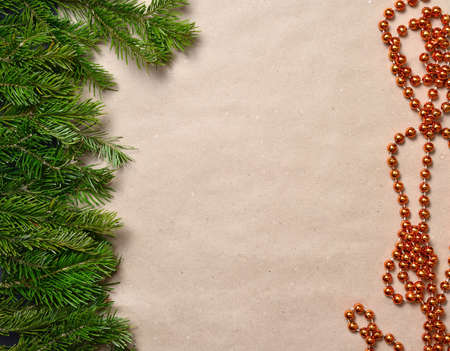 Background beige craft paper, at the left there is a strip of spruce green branches, right orange round beads to decorate the Christmas tree. Frame for text, inscriptions, empty space in the center.の写真素材