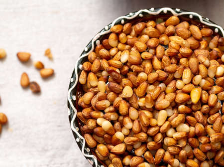 A bowl with peeled yellow Siberian pine nuts. Close-up top view. The background is blurred, a few...