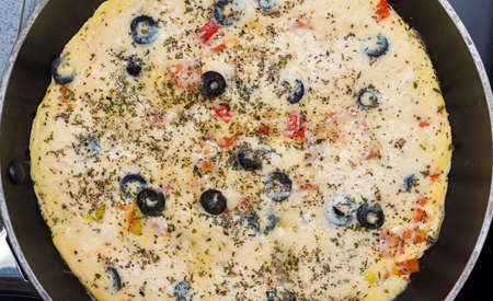 Cooked omelette in a round frying pan, top view. Eggs, milk, cheese, olives, tomatoes, spices. For...