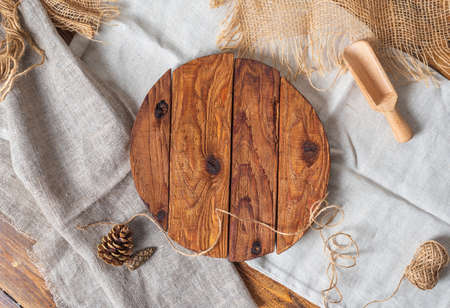 Round wooden cutting board made of rough boards on linen and burlap. Cones, a rope, a scoop for nuts lie nearby. Background with things from natural materials, top view, for recipes.の写真素材
