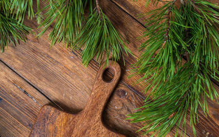 Fragment cutting board on a wooden table background surrounded by pine branches, top view. Empty space for menu text, recipes, eco-friendly style, forest background.の写真素材