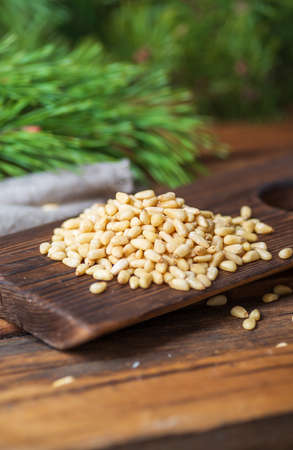 Peeled pine nuts are heaped on a dark wooden cutting board. In the background, sprawling branches of a green pine tree. Vertical.の写真素材