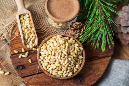 Pine nuts in a bowl, pine cone, branch, glass jar on a cutting board. Still life from natural...