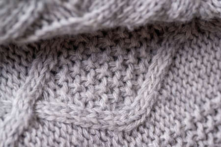Fragment of a knitted woolen plaid close-up. Gray threads, large knitting pattern in the form of a...