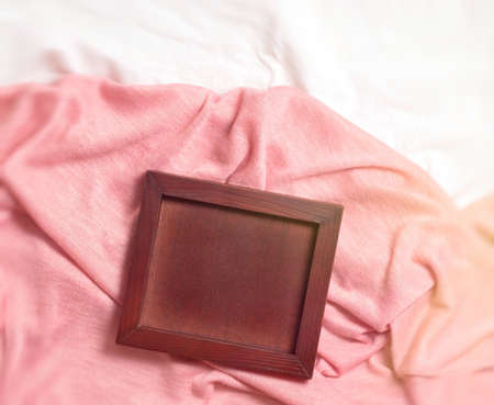 The wooden empty frame lies on the pink fabric with folds, the view from above. The background is...