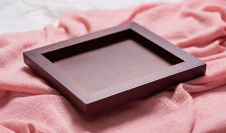 A wooden blank frame on a pink fabric sideways view. Empty space for text or photo, rectangular shape, lies on the soft surface of the knitted texture.の写真素材