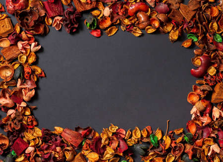 A frame of dry flowers on a black background. Dried petals, flowers and bark of red and orange flowers are poured around the perimeter of the photo, in the center an empty place for text, top view.の写真素材