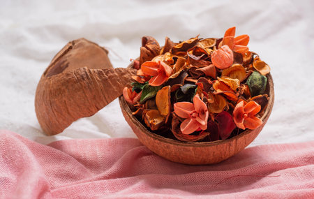 A coconut bowl with dried flowers and petals of buds on a pink and white fabric. Aromatherapy for the house on a hot summer day. Empty space for text, inscriptions.の写真素材
