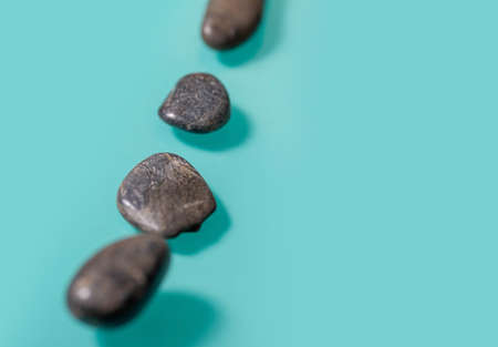 4 small black stones, similar to pebbles, lie diagonally on the left on a turquoise background....