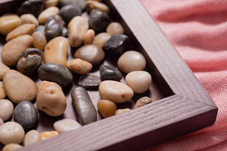 A wooden frame with sea pebbles on a pink fabric. Stones of two colors-light and dark. Empty space for text, inscriptions. The frame takes up a little space. The picture is pleasant to the eyes.の写真素材