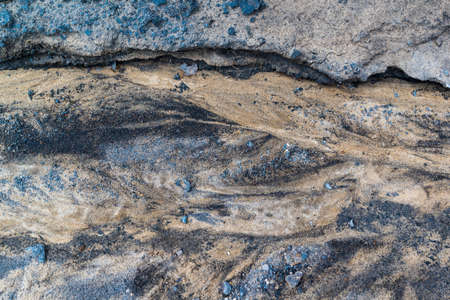 The texture is a close-up of the surface of the earth of sand and stones, blurred by a stream. Yellow and blue color of minerals, a pattern created by nature.の写真素材
