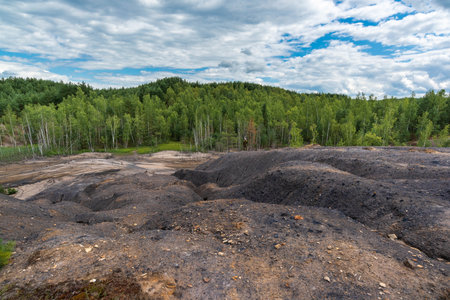 View from the top of the quarry hill to the dried up river, forest and sky with clouds. The surface of the earth is rocky dark, there are crevices. Russia, Tula region.の写真素材