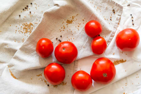 Red ripe tomatoes of light fabric, next to scattered grains of mustard and pepper. Background with fresh vegetables view from above.の写真素材