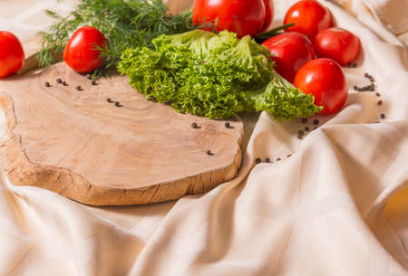 Fragment of cutting board made of olive tree, on which lie lettuce, dill, tomatoes. Pepper is scattered on the tablecloth. Ingredients for a salad of fresh vegetables.の写真素材