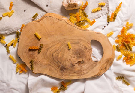 Cutting board curved shape of olive tree, scattered around pasta, garlic, pepper. They lie on a crud towel. Top view of the Italian cooking set.の写真素材