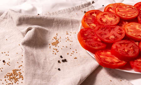 Plate with chopped tomatoes on a linen towel. Nearby scattered grains of mustard and pepper. Background about healthy food, vegetables, ready-made sliced dish.の写真素材