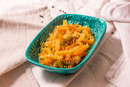 Turquoise rectangular ceramic plate with pasta of different colors. Stands on kitchen towels, side view close-up. Ideas for cooking in Italian style.の写真素材